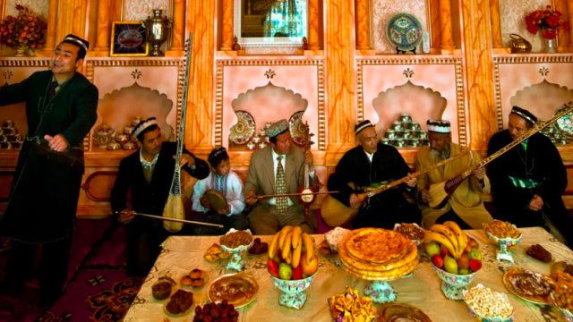 Traditional Uyghur musicians performing at a feast in Turpan, Xinjiang, with a table full of local food.