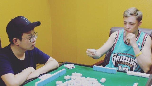 Two friends enjoying a traditional game of mahjong at a table, showcasing Chinese cultural heritage and strategy play.