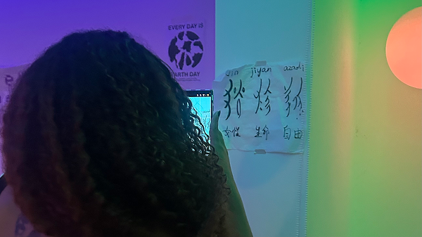 A traveler standing under neon lights, learning Nüshu — the secret written language historically used by women in Hunan, China.