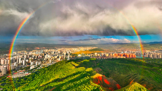 Panoramic view of Xining city with a vibrant rainbow arching over lush green mountains, highlighting the natural beauty of China’s summer capital.