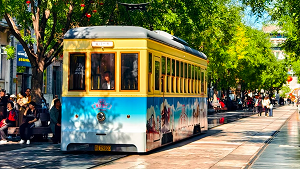 Historic yellow tram running along Qianmen Street in Beijing, surrounded by trees and tourists.