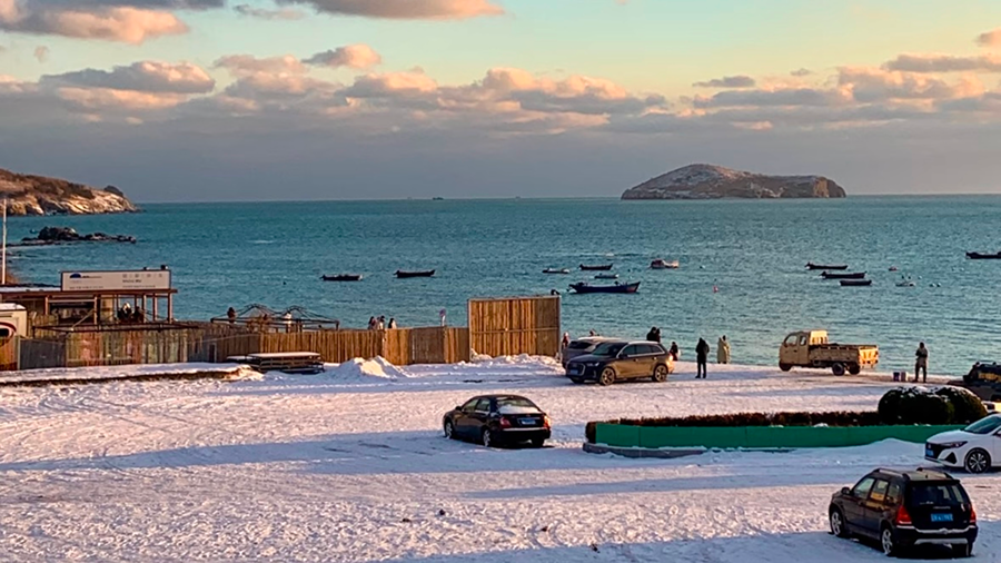 Winter seascape of Dalian coast in Liaoning, with fishing boats anchored near a small island under golden sunlight.