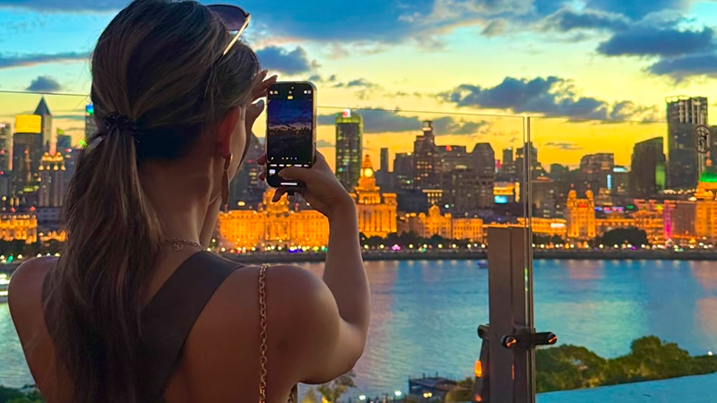 A girl capturing the night view of Shanghai with her mobile phone.