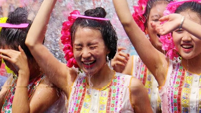 Young women in traditional Dai dresses joyfully splashed with water during Songkran Festival in Yunnan, celebrating the Southeast Asian New Year with smiles and vibrant floral garlands.