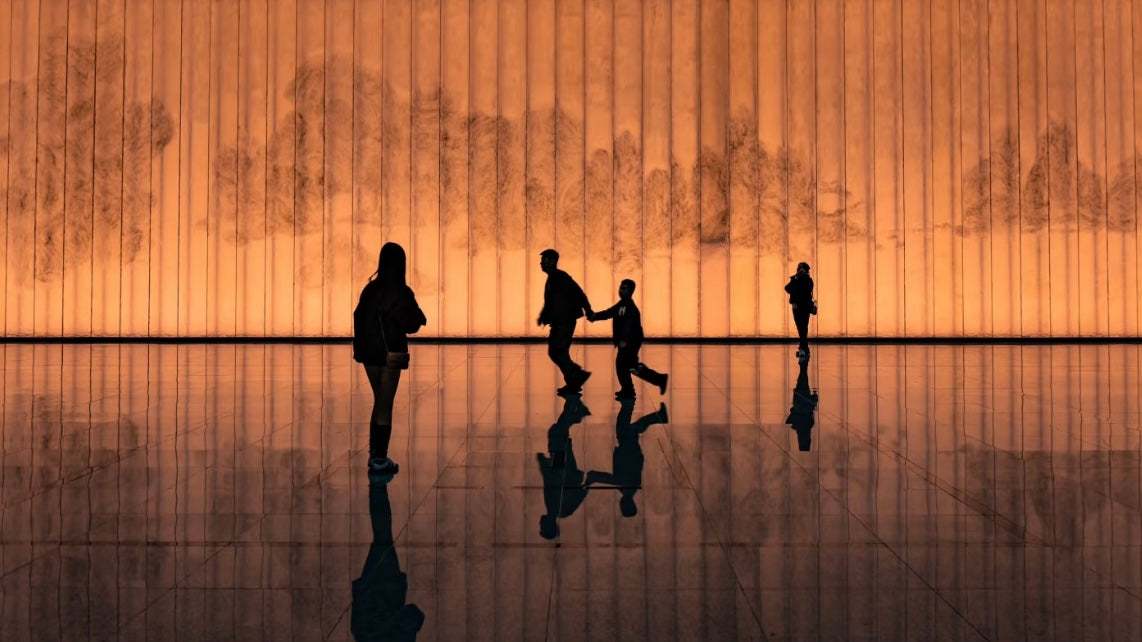 Visitors silhouetted against an illuminated wall featuring traditional Chinese landscape art at the Shanghai Museum, showcasing the blend of modern architecture and ancient culture.