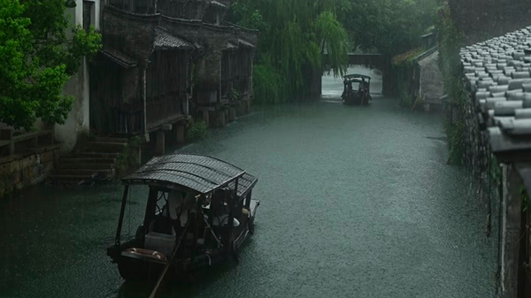 Traditional wooden boat sailing through a misty canal in Wuzhen Water Town during a rainy day.