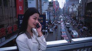 Businesswoman on Nanjing Road in 1990s Shanghai making a phone call above the bustling commercial street.