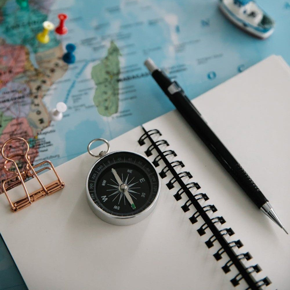 A notebook, compass, and world map with push pins, symbolizing expert-curated travel planning and local insights for China.