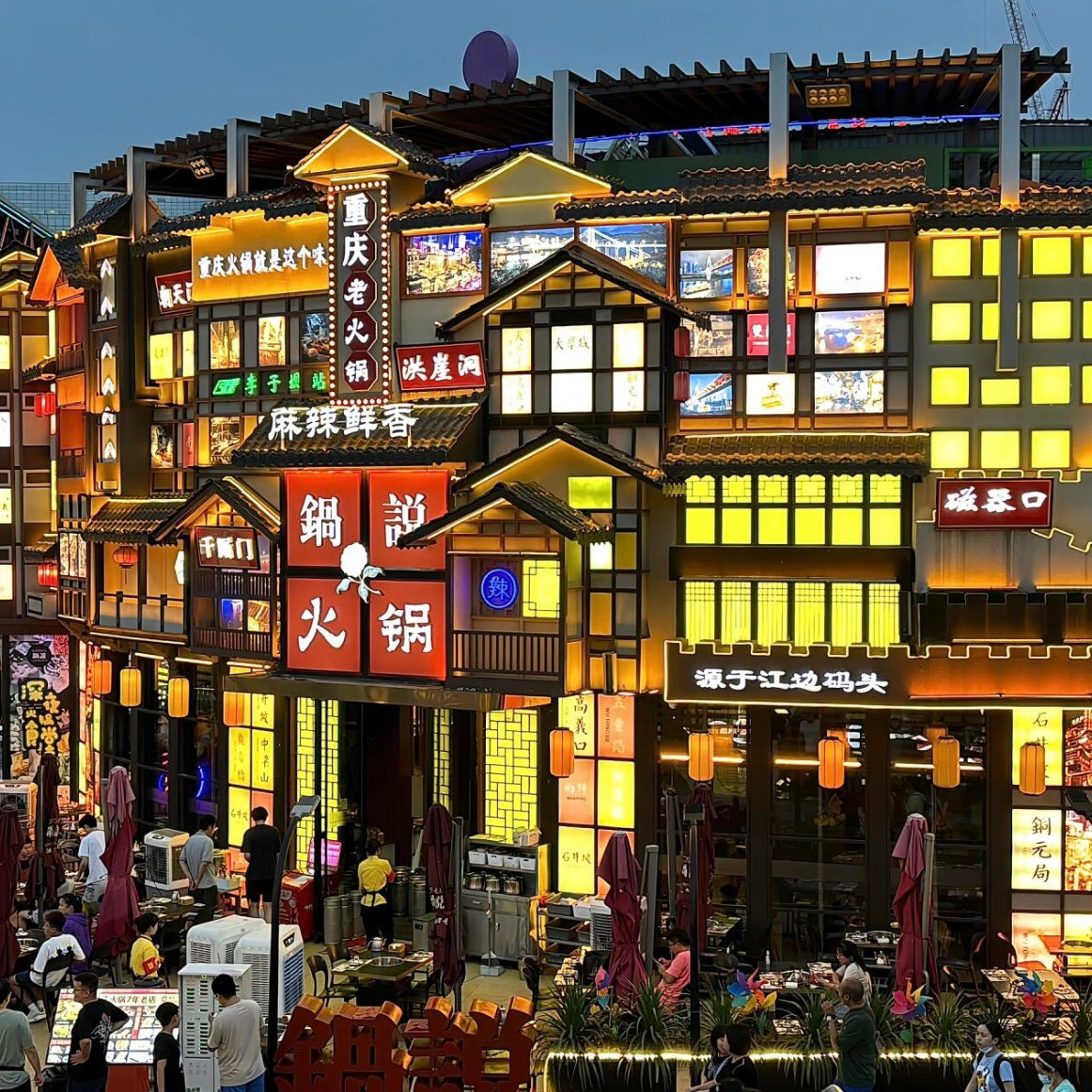 A lively night market in China with neon signs, traditional architecture, and bustling restaurants, showcasing local culture.