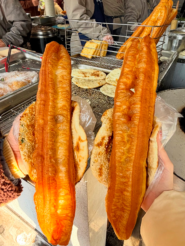 Two large crispy youtiao sticks freshly fried at a Hangzhou street breakfast stall