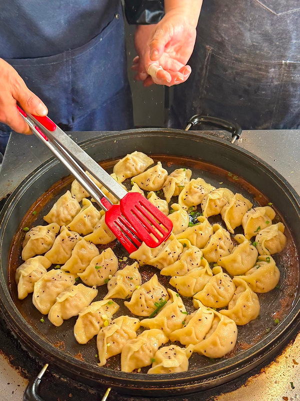 Fresh pan-fried soup dumplings cooking on a large skillet at Hangzhou morning market