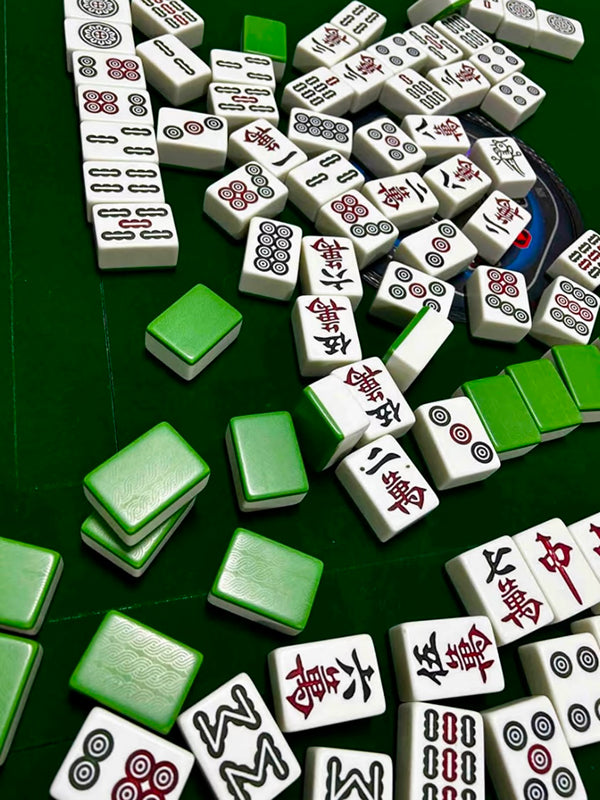 A collection of scattered Chinese mahjong tiles on a green table, highlighting the game's symbolic and artistic tile designs