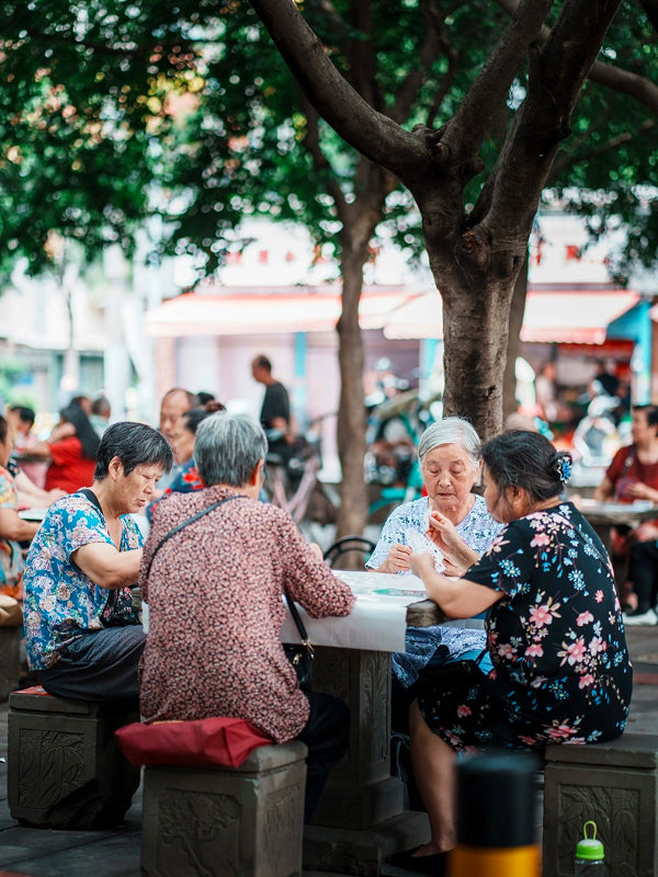 Elderly Chengdu residents gathered around a stone table playing cards under shade trees, showcasing strong community bonds
