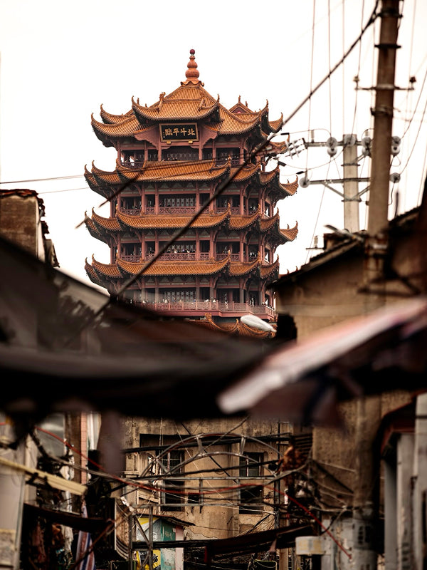 Iconic Yellow Crane Tower rising above the rooftops and tangled wires of an old Wuhan neighborhood, blending culture with reality