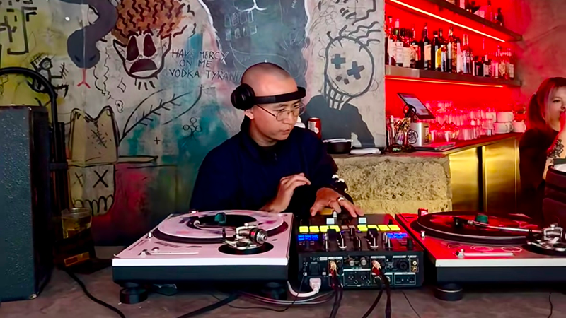 A shaven-headed DJ at a Chengdu bar is working the decks with intense energy.