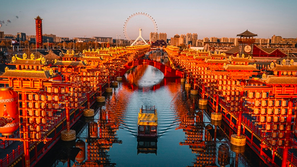 Stunning view of Hebei’s Grand Canal illuminated by red lanterns at sunset, with a boat sailing through and a ferris wheel in the background, showcasing the cultural charm of northern China.