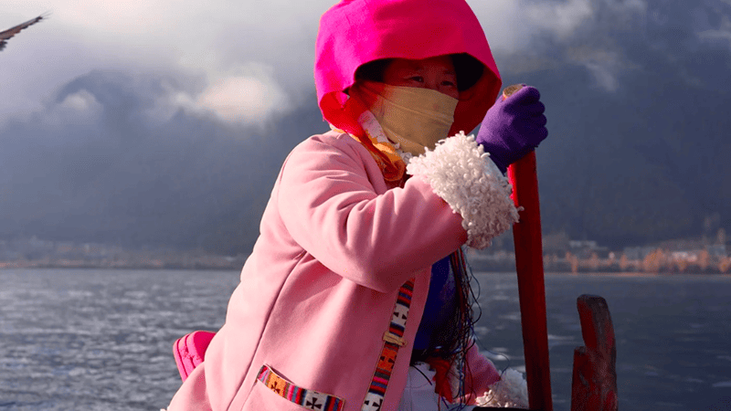 A woman's rowing a boat on Lugu Lake.
