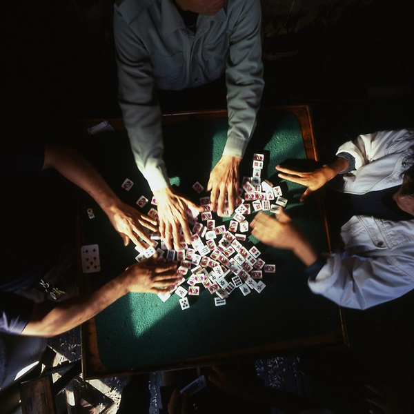 Multiple hands scrambling Mahjong tiles at the start of a lively game session.