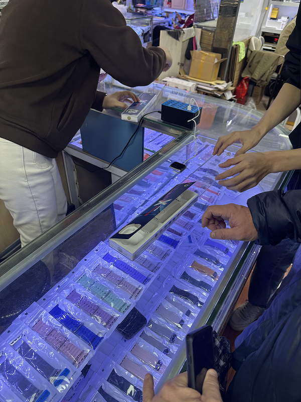 Customer browsing smartphone screen protectors under LED-lit display case in Huaqiangbei