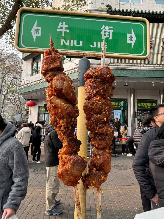 Skewered halal lamb kebabs grilled to perfection under the Niujie Street sign, a famous halal food destination in Beijing