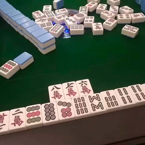 Close-up of a mahjong game in progress on a green table showing Chinese character tiles and circles in a Chengdu setting.