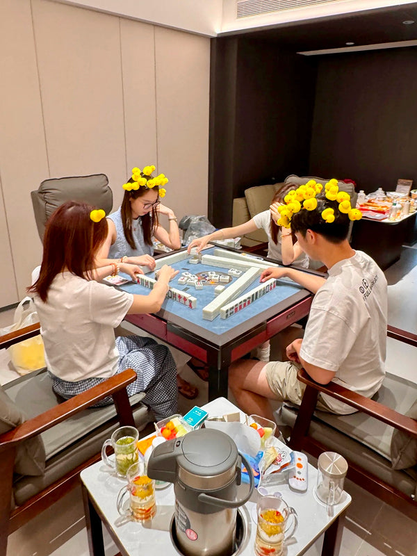 Group of young adults playing traditional Chinese mahjong indoors in Chengdu, enjoying tea and snacks during a cultural experience