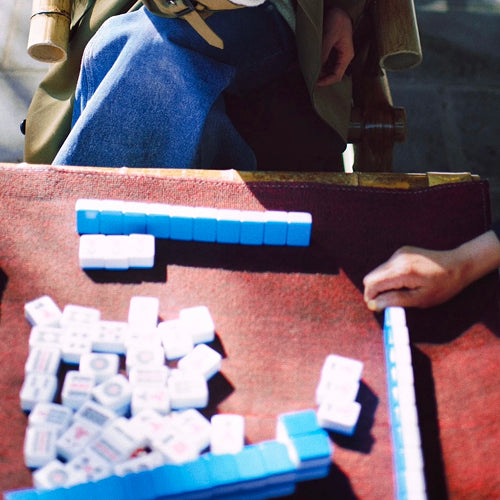 Outdoor mahjong game in Chengdu with players using blue and white tiles on a red felt table in natural daylight.