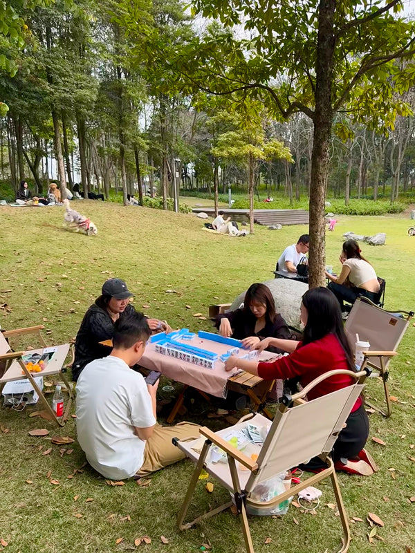 Friends enjoying a traditional mahjong game outdoors in a scenic Beijing park, combining leisure and Chinese culture