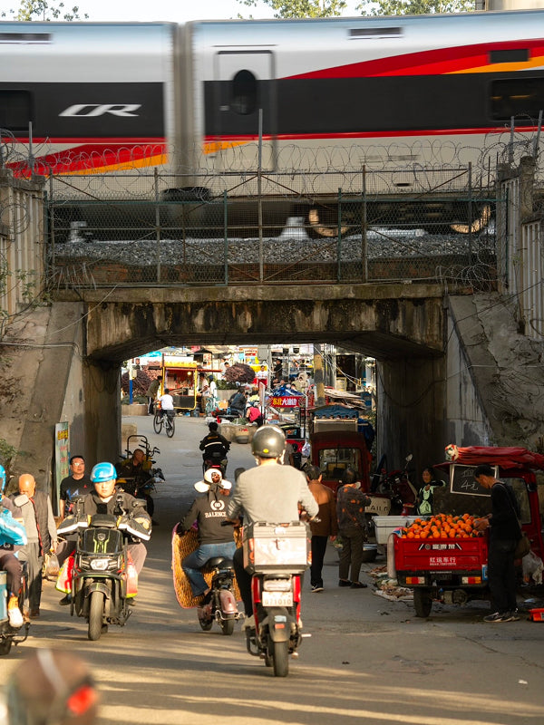 Fast train crossing above a bustling Chengdu underpass filled with scooters, vendors, and vibrant street market activity