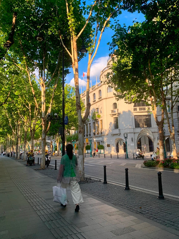Woman strolling through a shaded, tree-lined avenue in Wuhan’s historic French Concession-style neighborhood during sunset