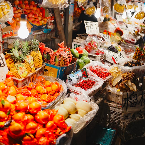 Colorful fruit stand at a Wuhan night market, showcasing tropical fruits like pineapples, durians, and persimmons under warm lights.