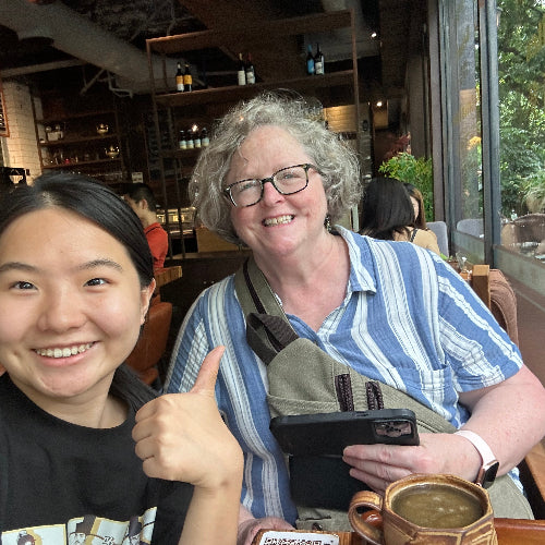 Local Chengdu resident taking a cheerful selfie with a foreign traveler inside a cozy coffee shop.